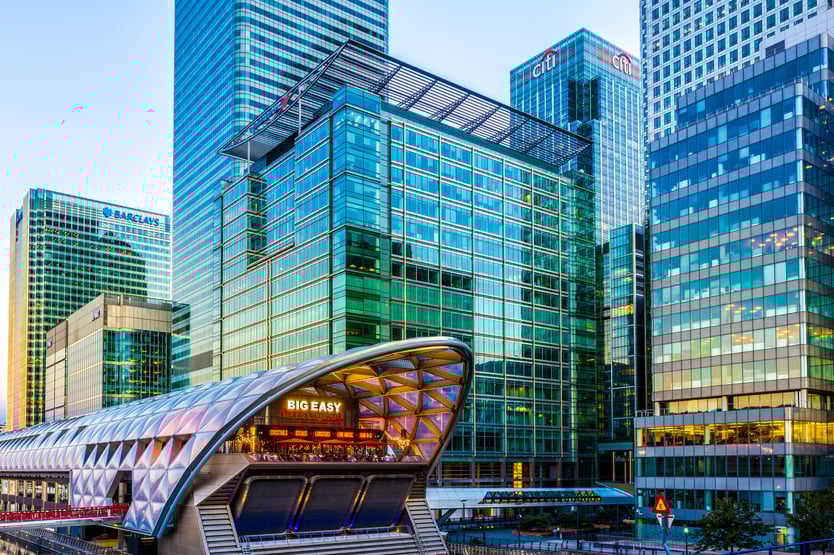 London, UK, View of Canary Wharf office buildings at dusk from across the North Dock, with illuminated Crossrail station in the foreground